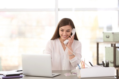 Photo of Young woman talking on phone at workplace