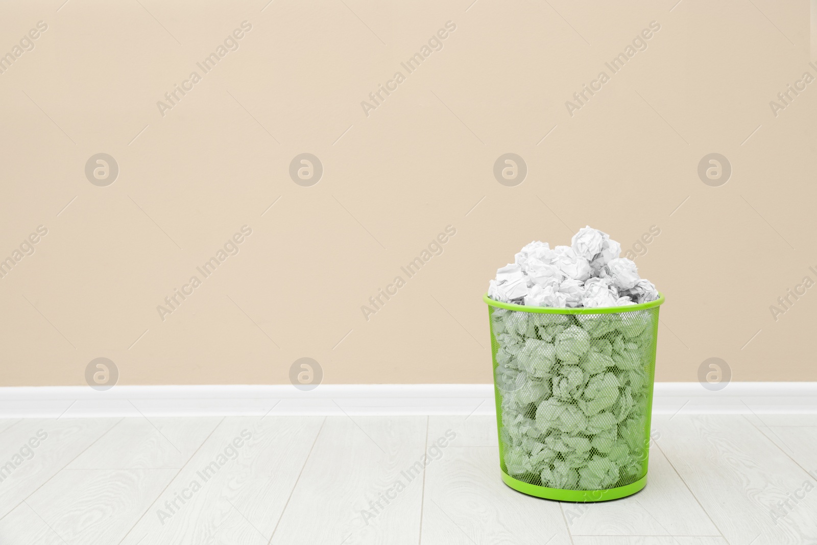 Photo of Metal bin with crumpled paper against color wall, space for text