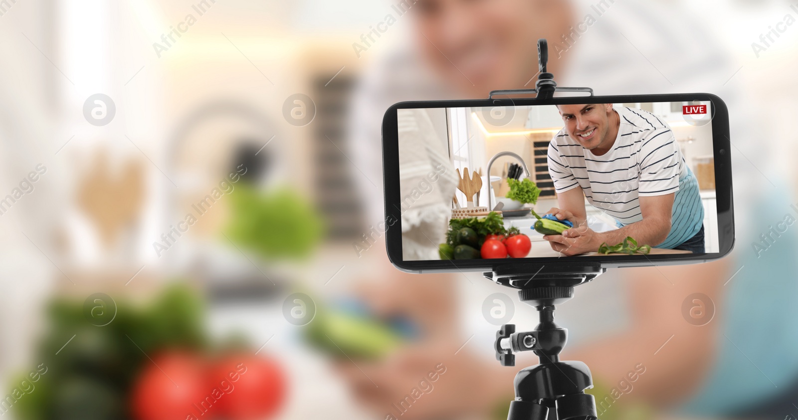 Image of Man peeling cucumber at kitchen counter, selective focus on smartphone display