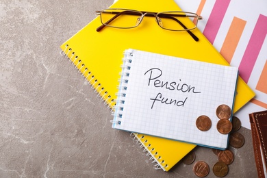 Photo of Flat lay composition with stationery, coins, glasses and words PENSION FUND written in notebook on table