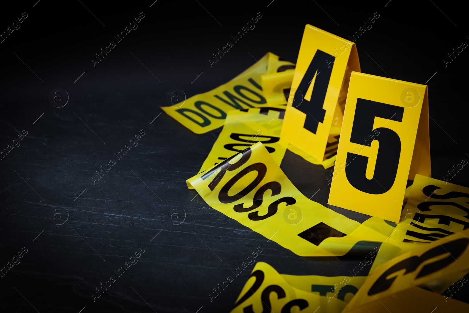 Photo of Crime scene tape and evidence markers on black slate background, closeup. Space for text