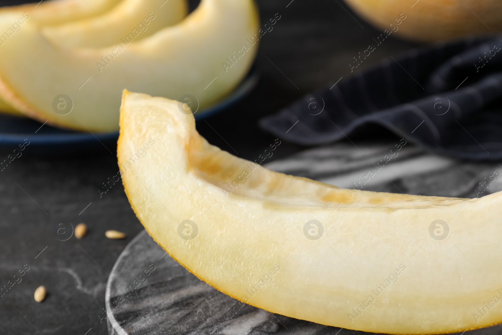 Photo of Slice of delicious honeydew melon on grey marble board, closeup