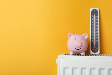 Photo of Piggy bank and thermometer on heating radiator against orange background, space for text