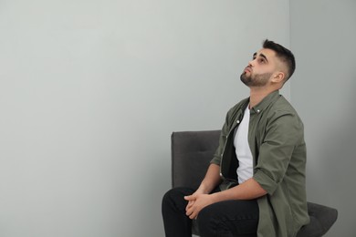 Photo of Sad man sitting near light grey wall. Space for text