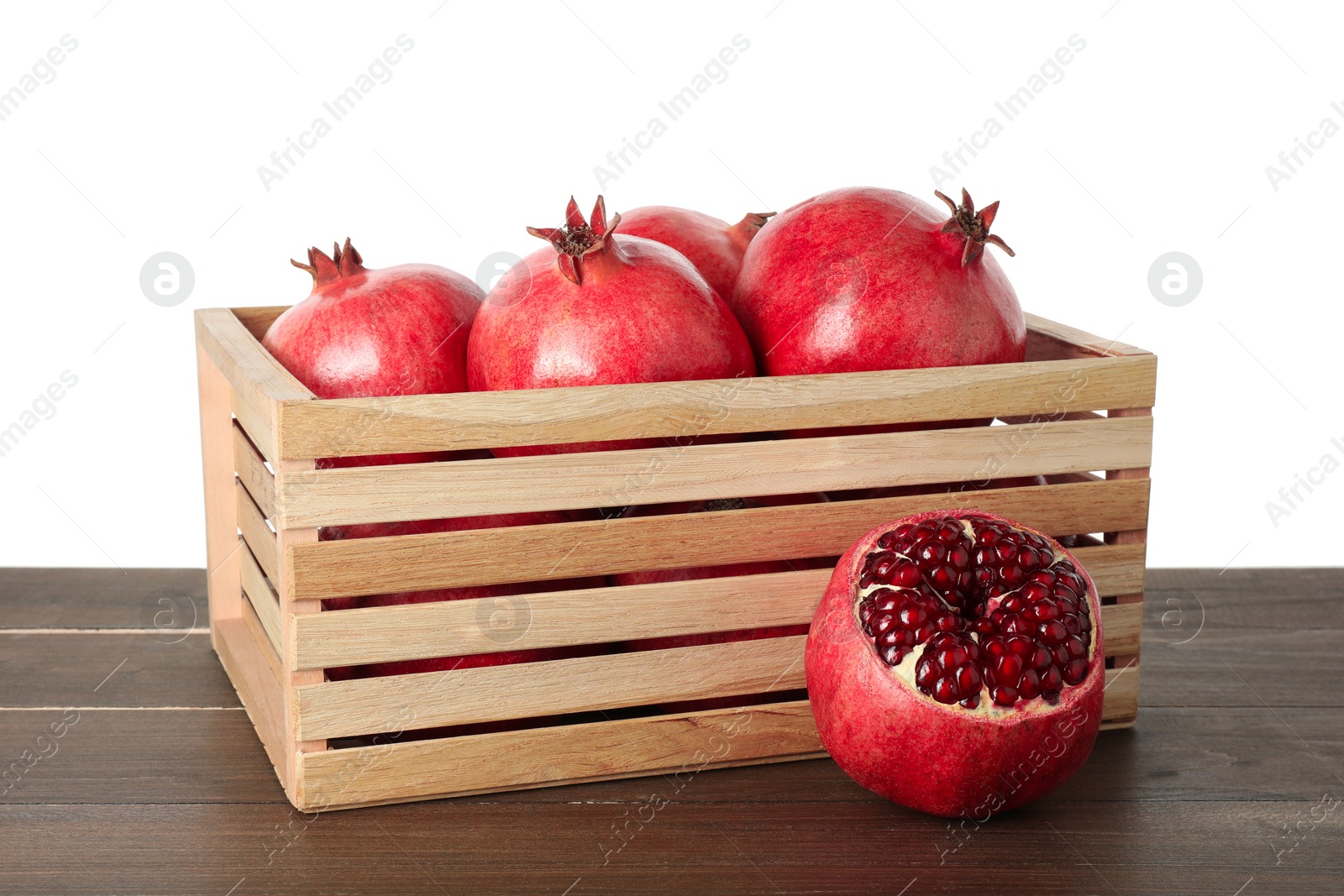 Photo of Fresh pomegranates in crate on wooden table against white background