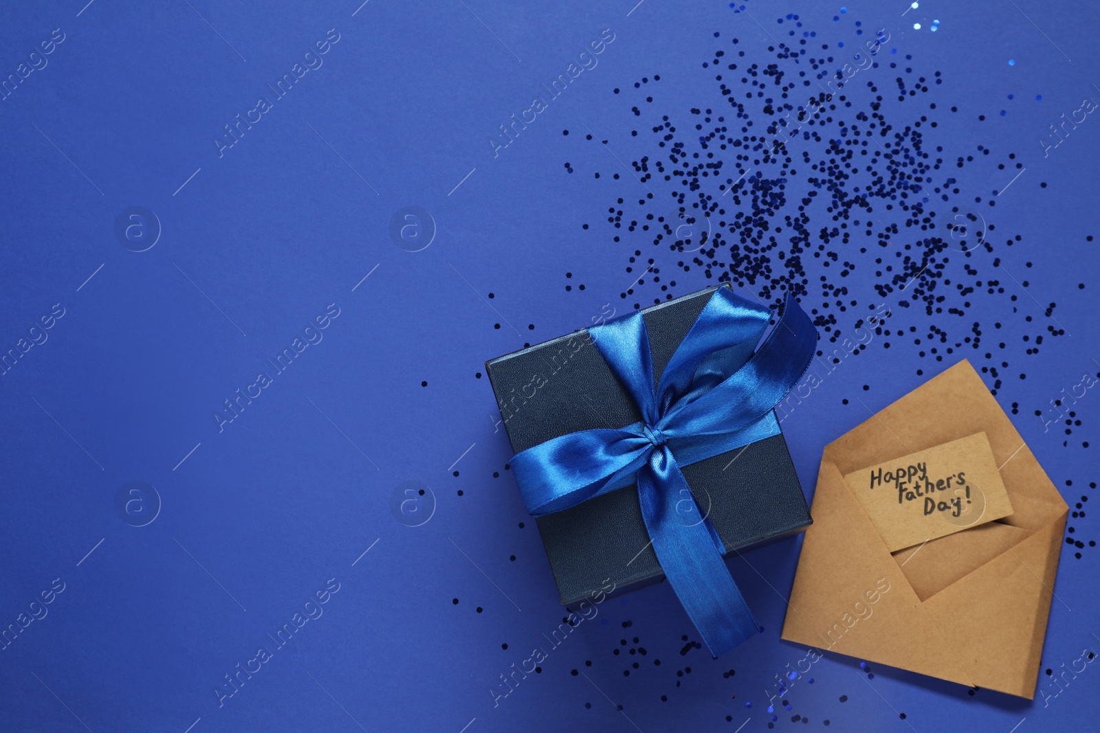 Photo of Card with phrase Happy Father's Day, gift box and confetti on blue background, flat lay. Space for text