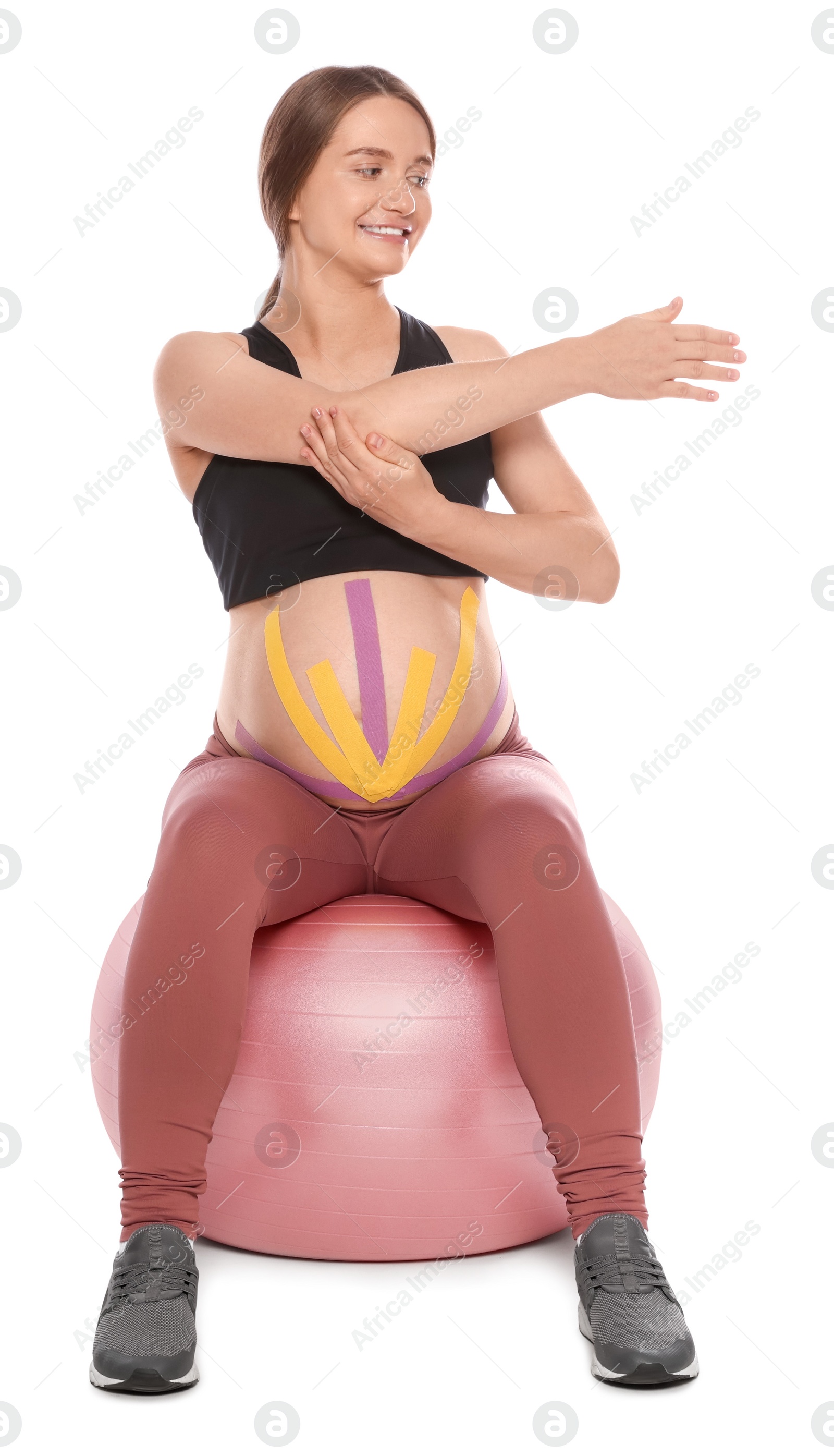 Photo of Sporty pregnant woman with kinesio tapes doing exercises on fitball against white background