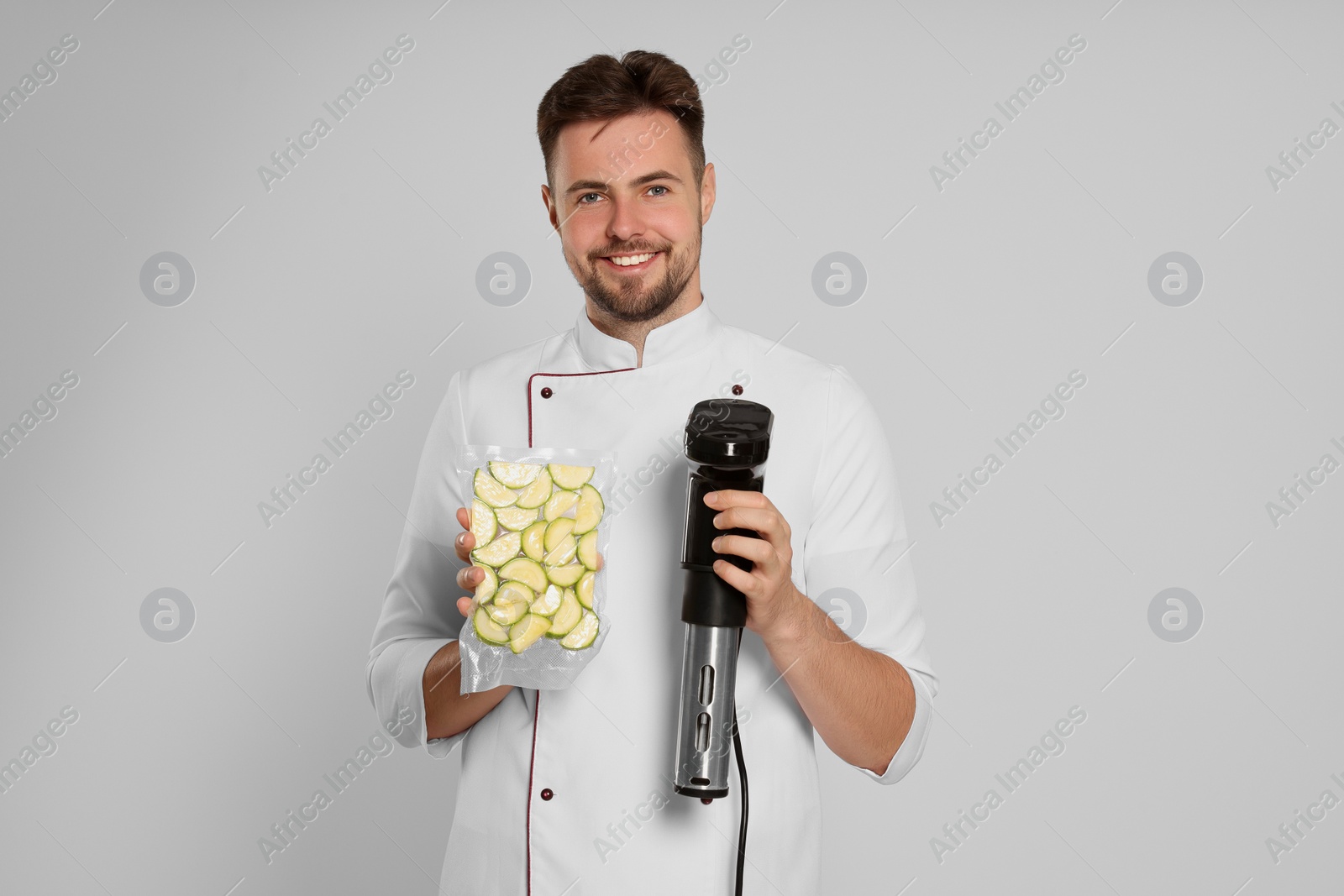 Photo of Chef holding sous vide cooker and zucchini in vacuum pack on beige background