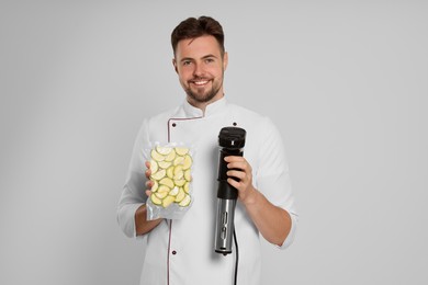 Photo of Chef holding sous vide cooker and zucchini in vacuum pack on beige background
