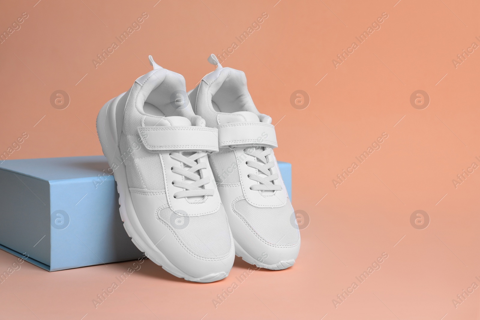 Photo of Pair of comfortable sports shoes and box on pale coral background. Space for text