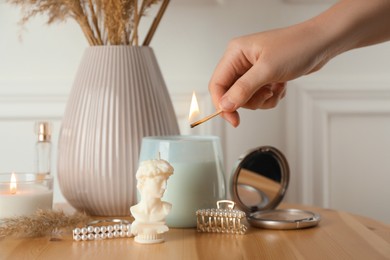 Photo of Woman lighting David bust candle on wooden table, closeup. Stylish decor