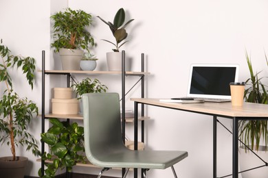 Photo of Beautiful workplace with laptop on wooden table, chair and houseplants in room