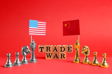 Photo of Wooden cubes with words Trade War, chess pieces, American and Chinese flags on red background