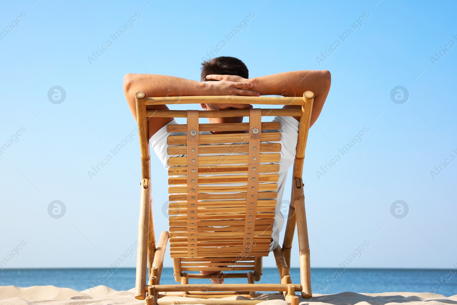 Photo of Young man relaxing in deck chair on sandy beach