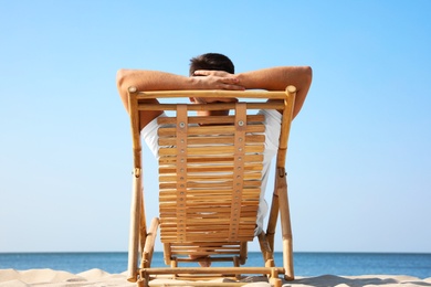 Young man relaxing in deck chair on sandy beach