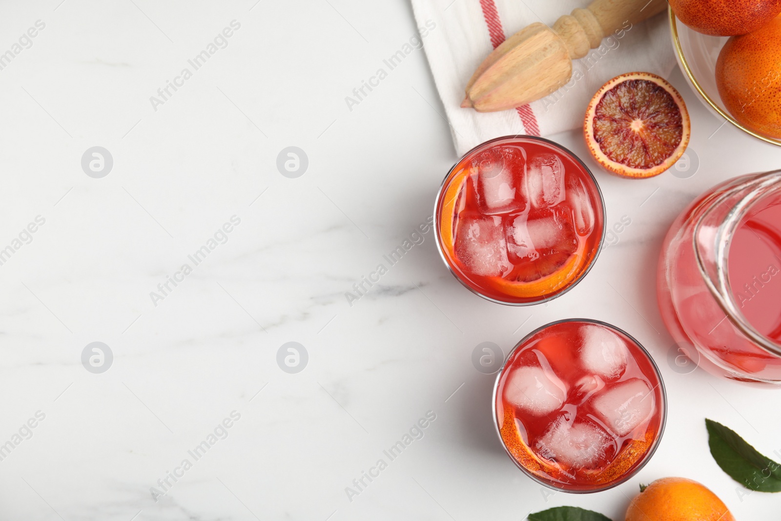 Photo of Tasty sicilian orange juice with ice cubes, fruits and squeezer on white marble table, flat lay. Space for text
