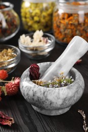 Photo of Mortar with pestle and many different herbs on wooden table, closeup