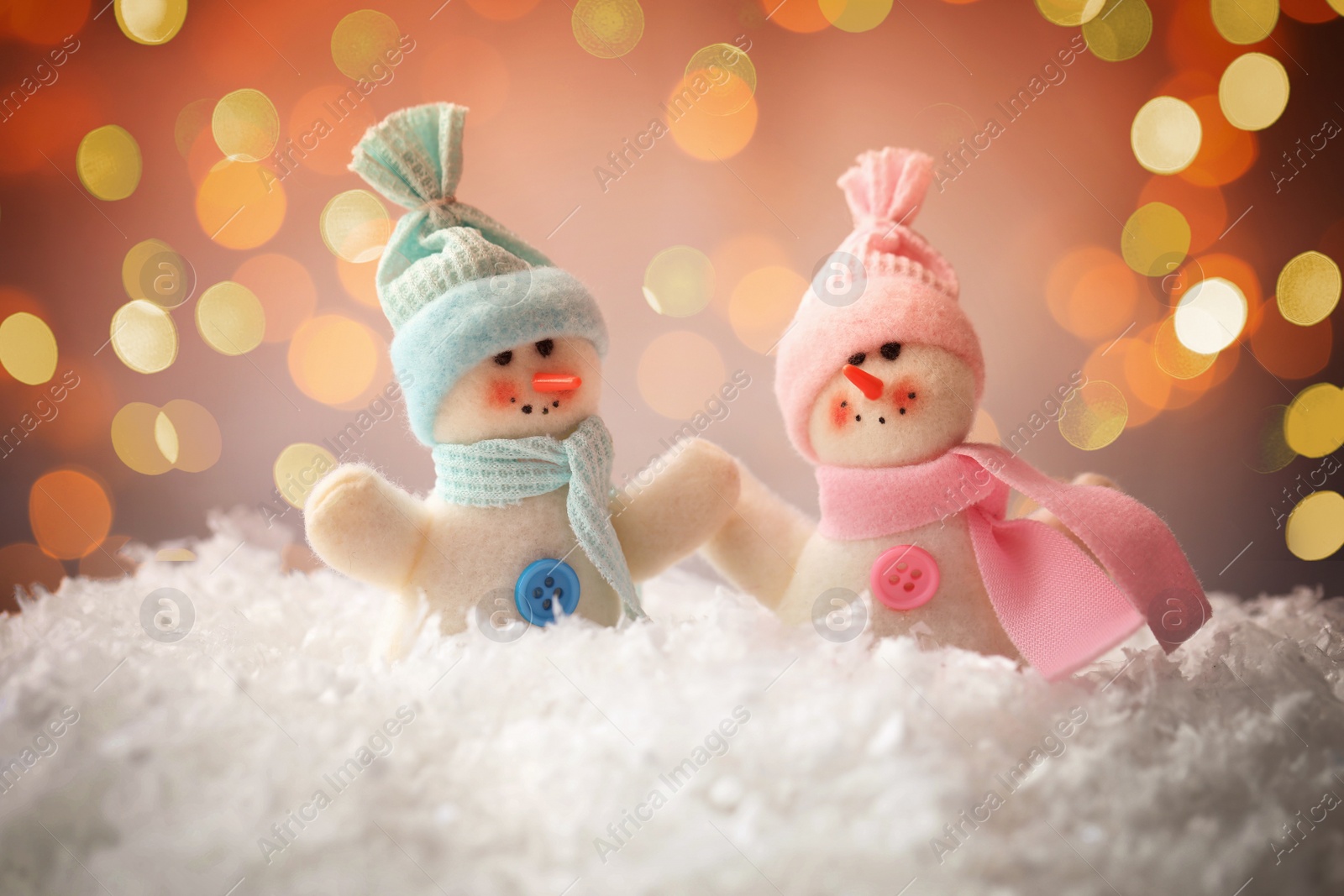 Image of Cute snowmen in snow against blurred Christmas lights on background