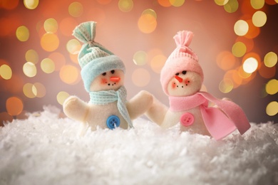 Image of Cute snowmen in snow against blurred Christmas lights on background