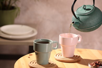 Pouring aromatic tea into cup at wooden table