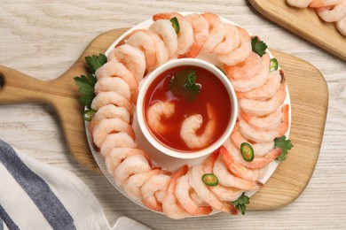 Photo of Tasty boiled shrimps with cocktail sauce, chili and parsley on light wooden table, flat lay
