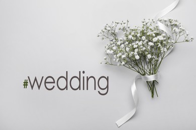 Beautiful bouquet of white gypsophila flowers with ribbon and hashtag Wedding on light grey background, top view.