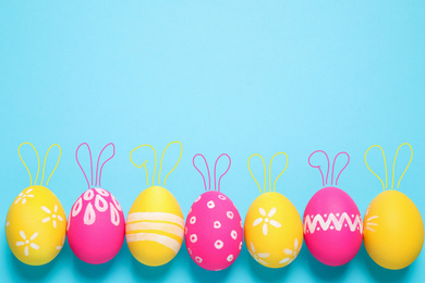 Image of Bright Easter eggs with cute bunny ears and space for text on light blue background, flat lay