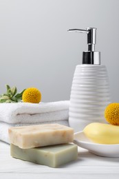 Soap bars, bottle dispenser and towels on wooden table against white background