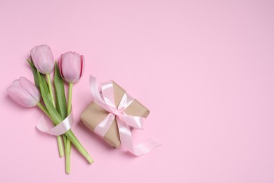 Photo of Beautiful gift box with bow and tulips on pink background, flat lay. Space for text