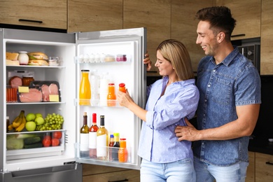 Photo of Couple taking bottle with juice out of refrigerator in kitchen