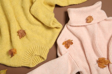 Photo of Warm sweaters and dry leaves on brown background, flat lay. Autumn season