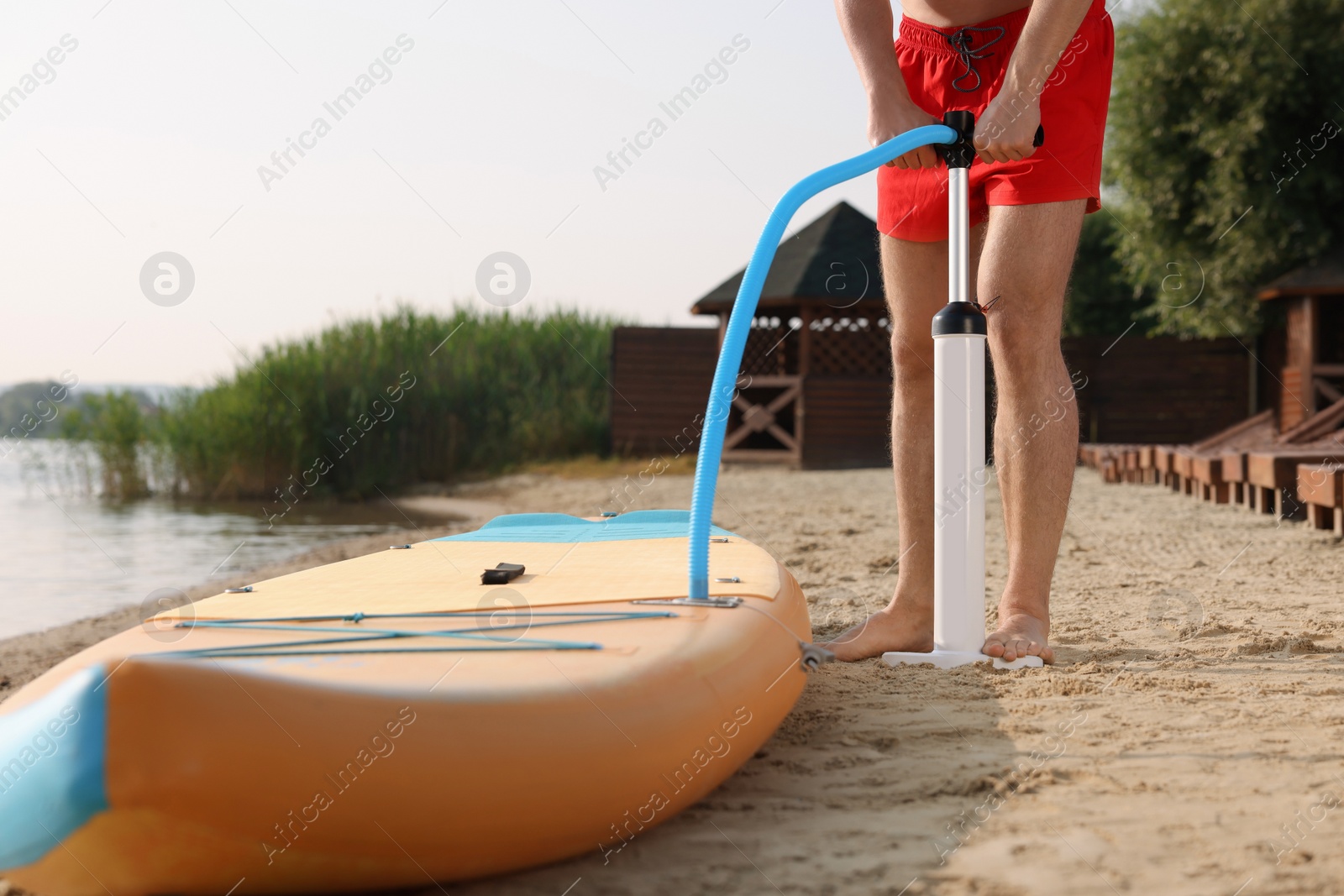 Photo of Man pumping up SUP board on river shore, closeup