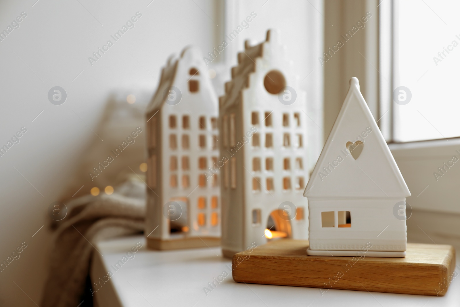 Photo of Beautiful house shaped candle holders and festive lights on windowsill indoors, space for text