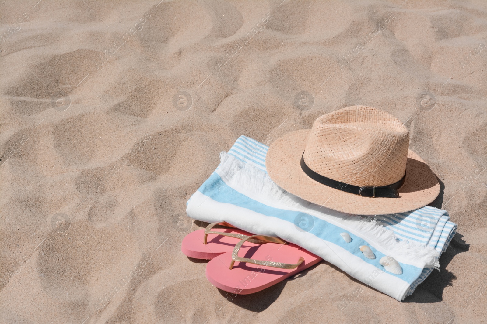 Photo of Straw hat, beach towel, seashells and flip flops on sand, space for text