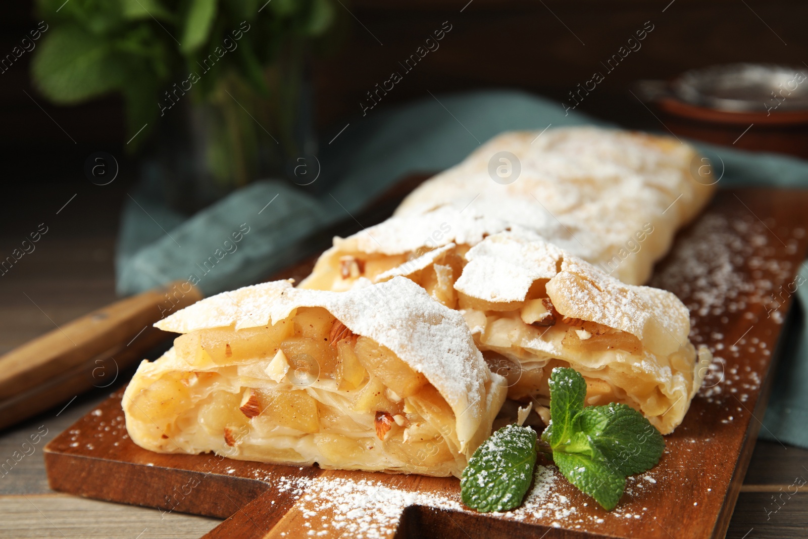 Photo of Delicious apple strudel with almonds, powdered sugar and mint on wooden board, closeup