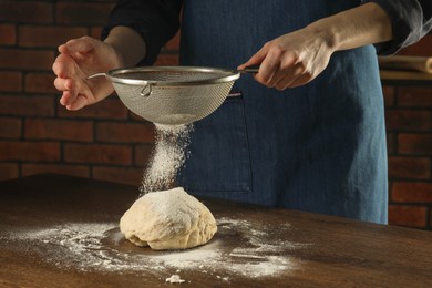 Making bread. Woman sprinkling flour onto dough at wooden table indoors, closeup