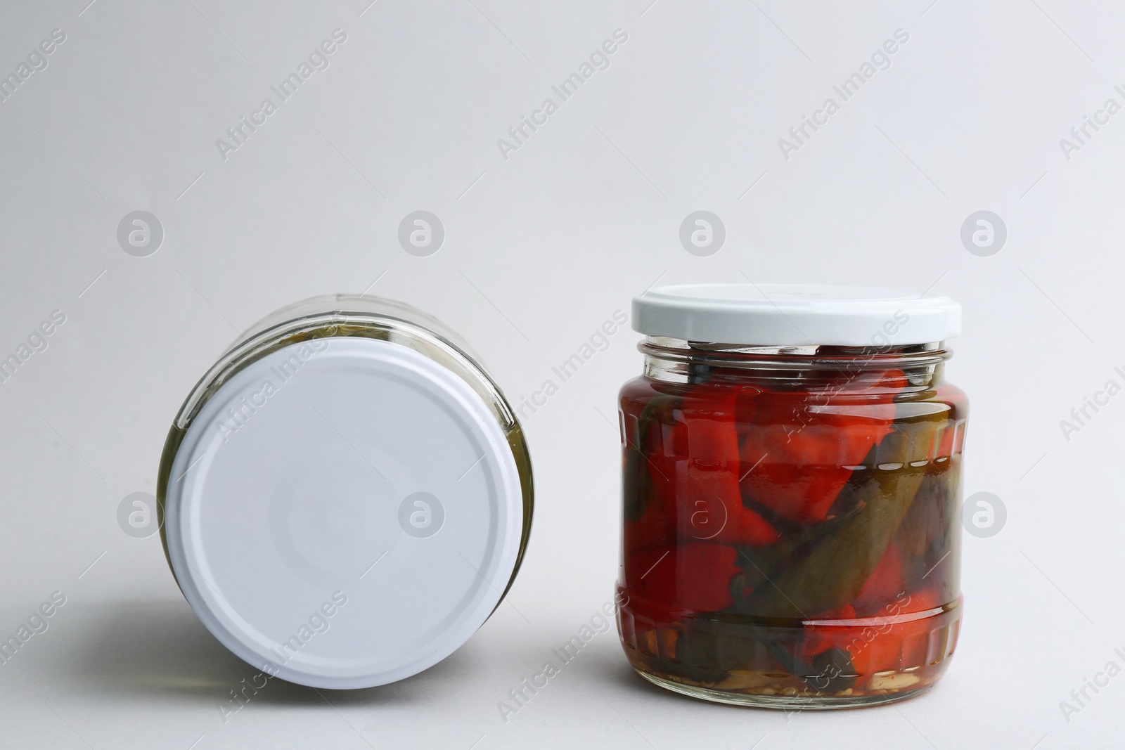 Photo of Glass jars with pickled bell peppers and cucumbers on white background
