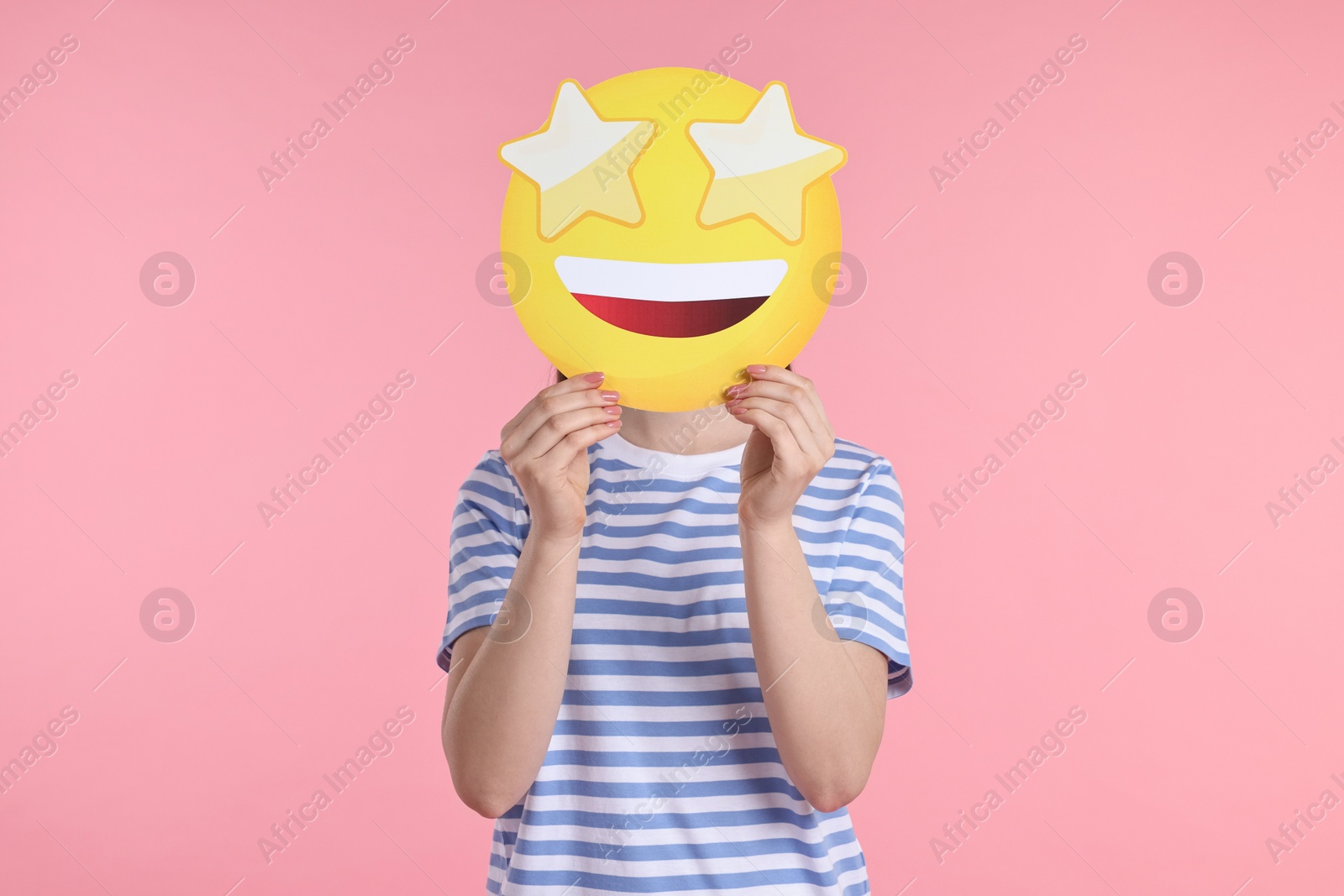 Photo of Woman holding emoticon with stars instead of eyes on pink background
