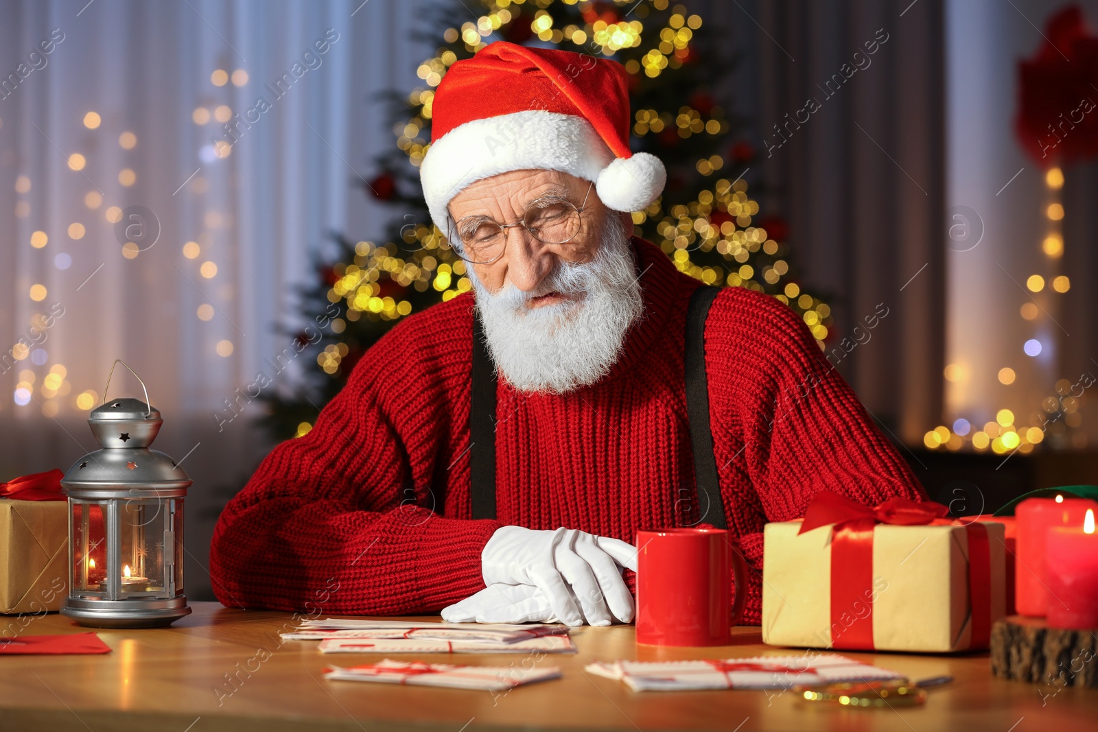 Photo of Santa Claus reading letter at his workplace in room decorated for Christmas