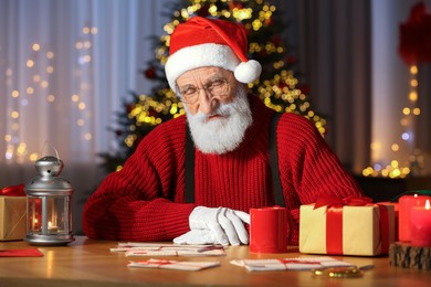 Photo of Santa Claus reading letter at his workplace in room decorated for Christmas