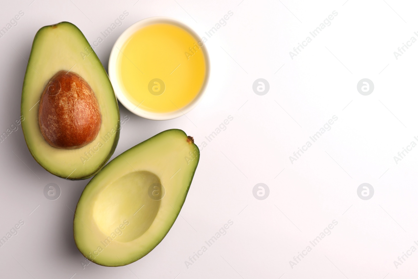 Photo of Cooking oil in bowl and fresh avocados on white background, flat lay. Space for text