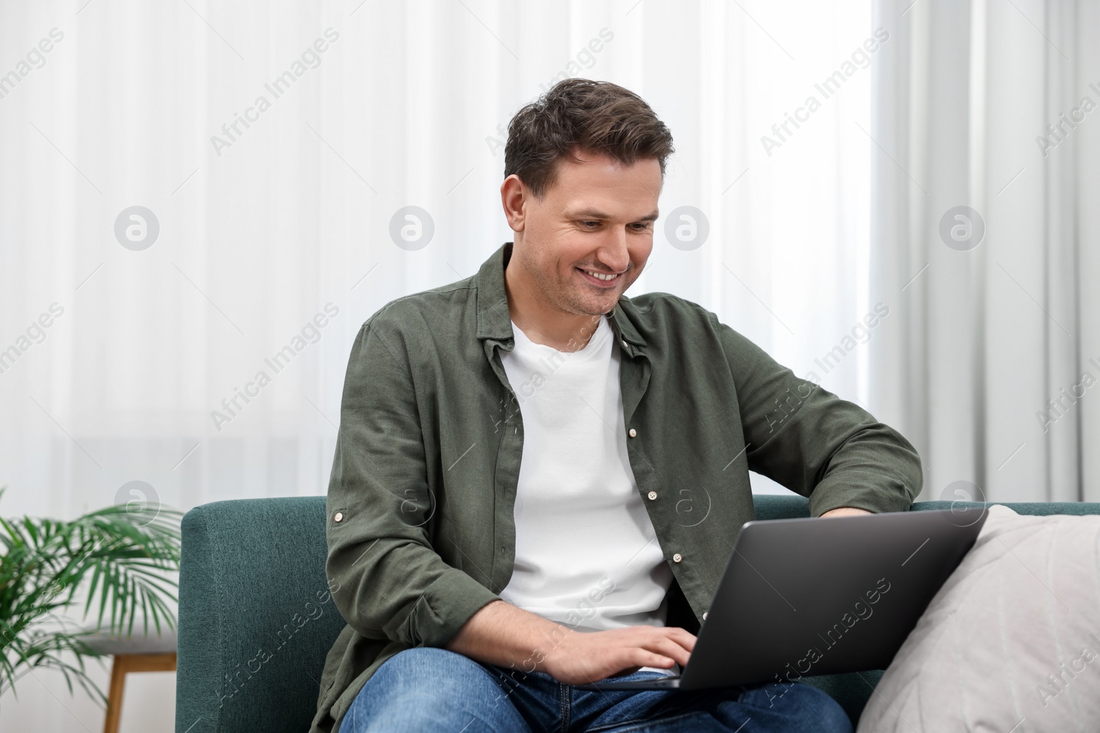 Photo of Happy man using laptop on sofa at home