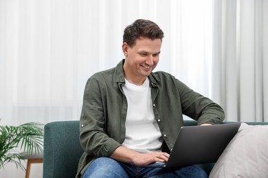 Photo of Happy man using laptop on sofa at home