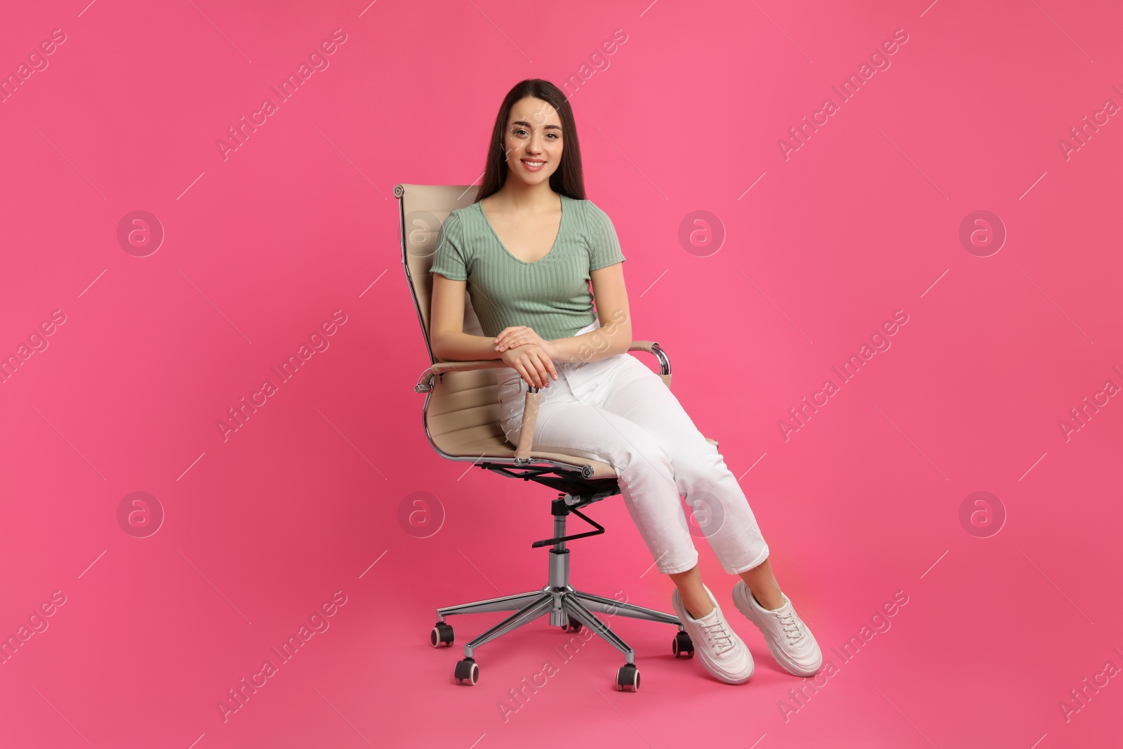 Photo of Young woman sitting in comfortable office chair on pink background