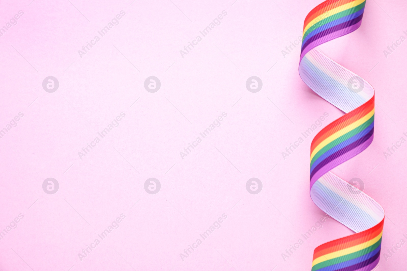 Photo of Top view of rainbow ribbon on pink background, space for text. Gay symbol