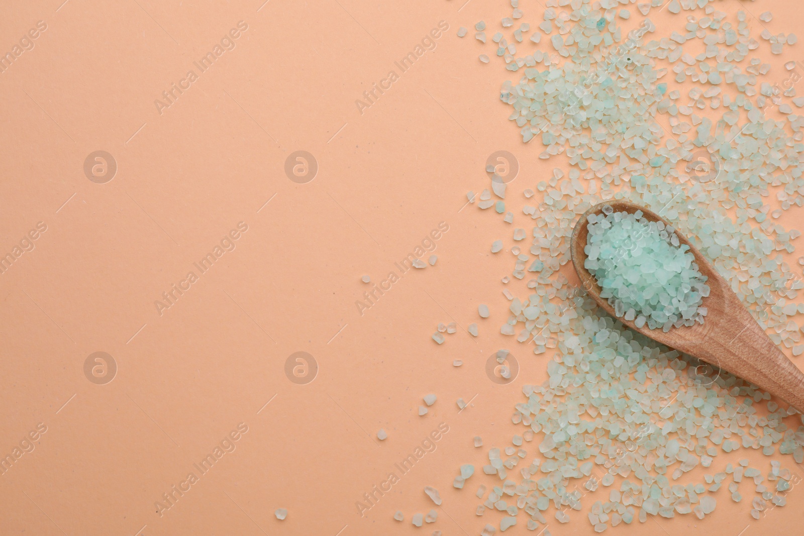 Photo of Spoon with turquoise sea salt on beige background, top view. Space for text