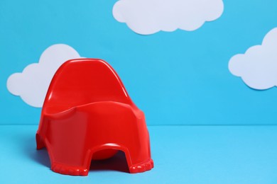 Photo of Red baby potty against light blue background with paper clouds, space for text. Toilet training