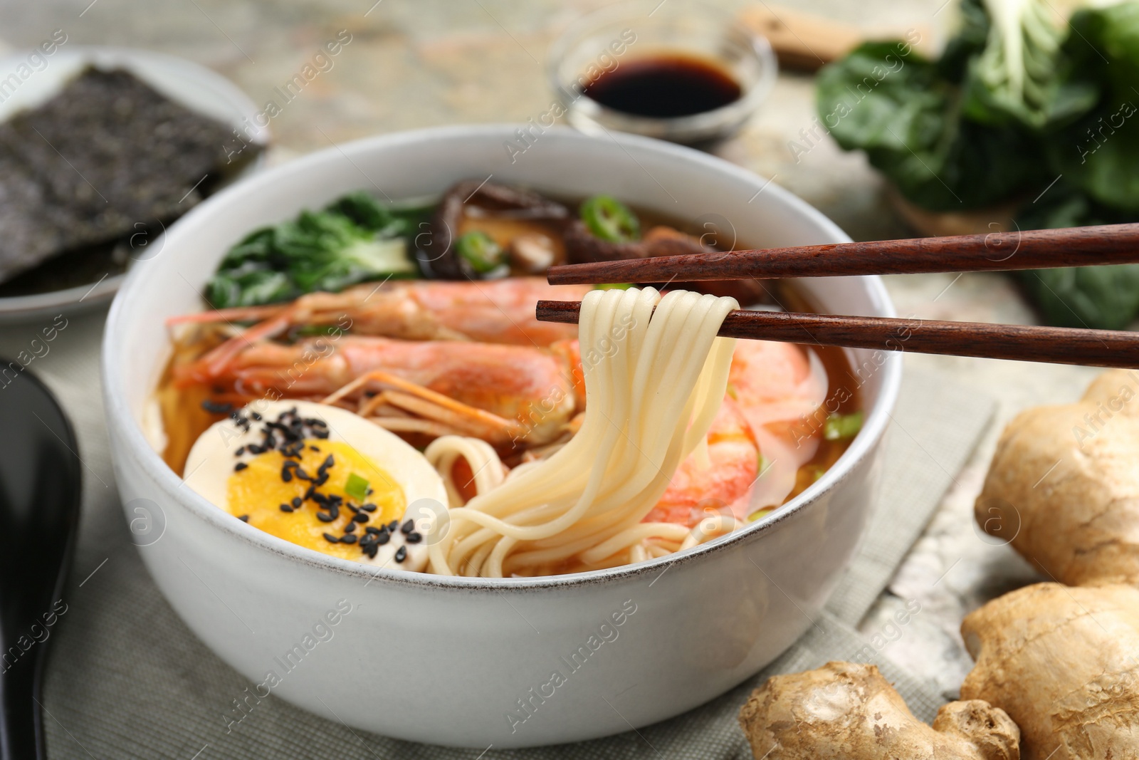 Photo of Eating delicious ramen from bowl with chopsticks at table, closeup. Noodle soup