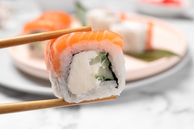 Photo of Chopsticks with tasty sushi roll on blurred background, closeup