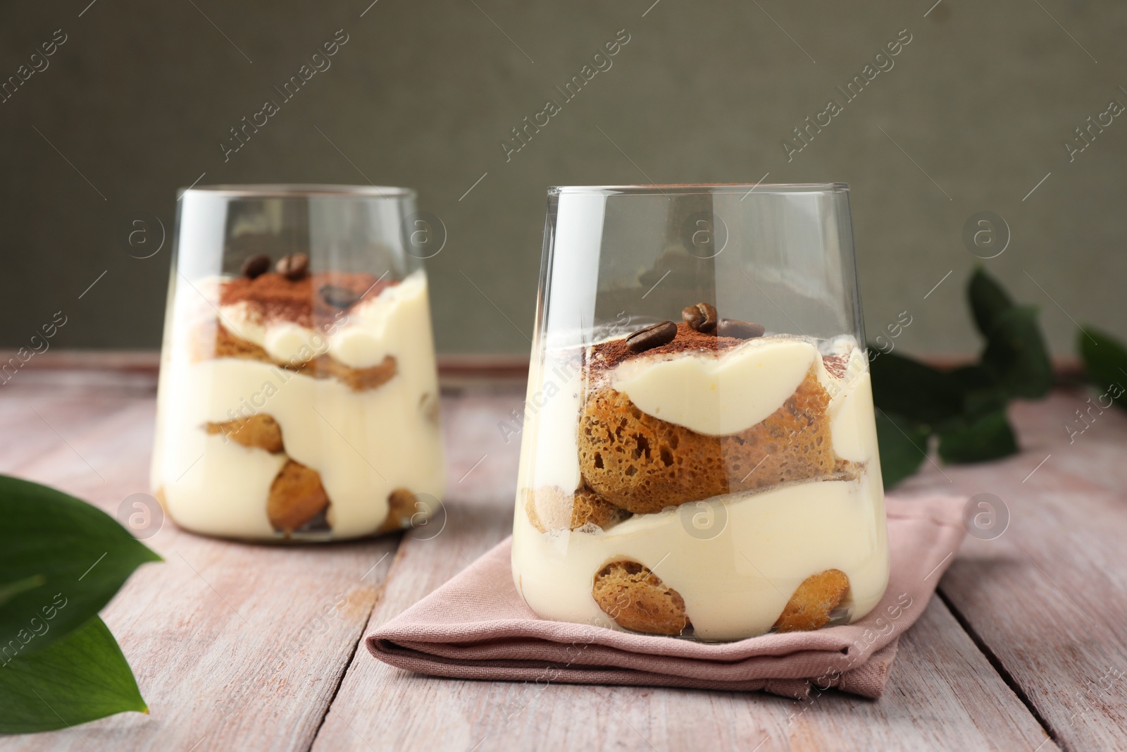 Photo of Delicious tiramisu with coffee beans in glasses and green leaves on wooden table